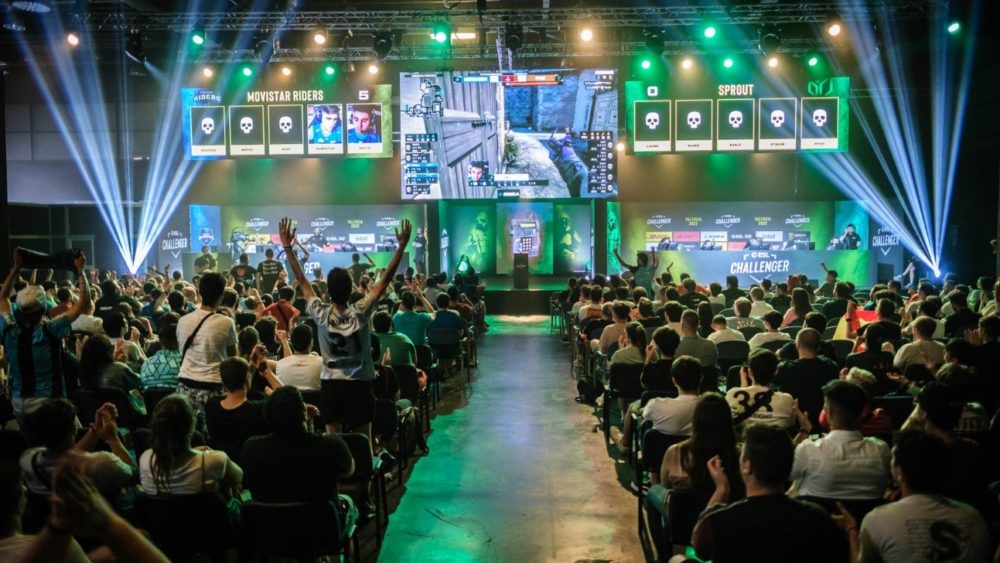 Foto de un evento DreamHack con personas sentadas de espaldas viendo una competición de un videojuego en una pantalla grande.