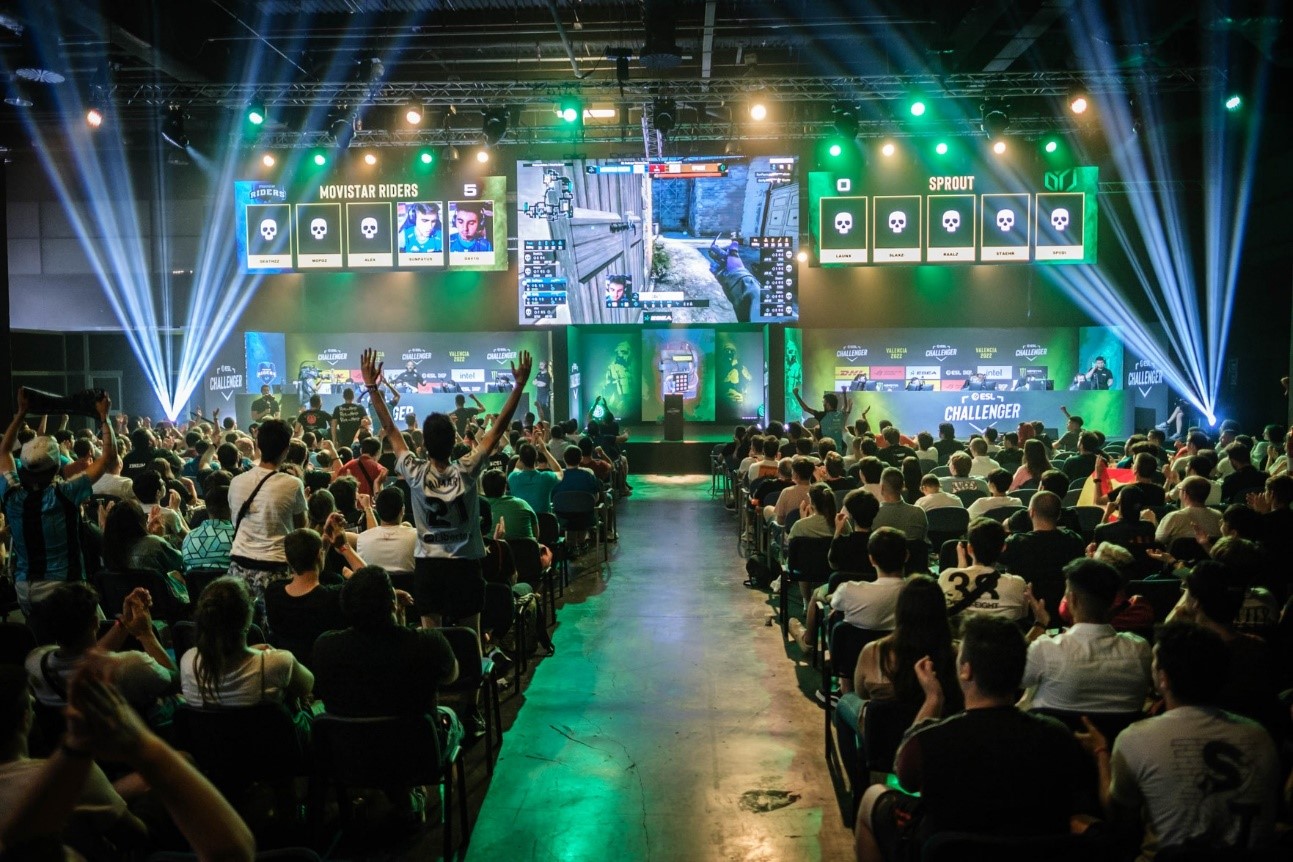 Foto de un evento DreamHack con personas sentadas de espaldas viendo una competición de un videojuego en una pantalla grande.